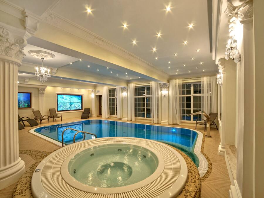 Una piscina interior de lujo con jacuzzi, elegantes columnas y una araña.