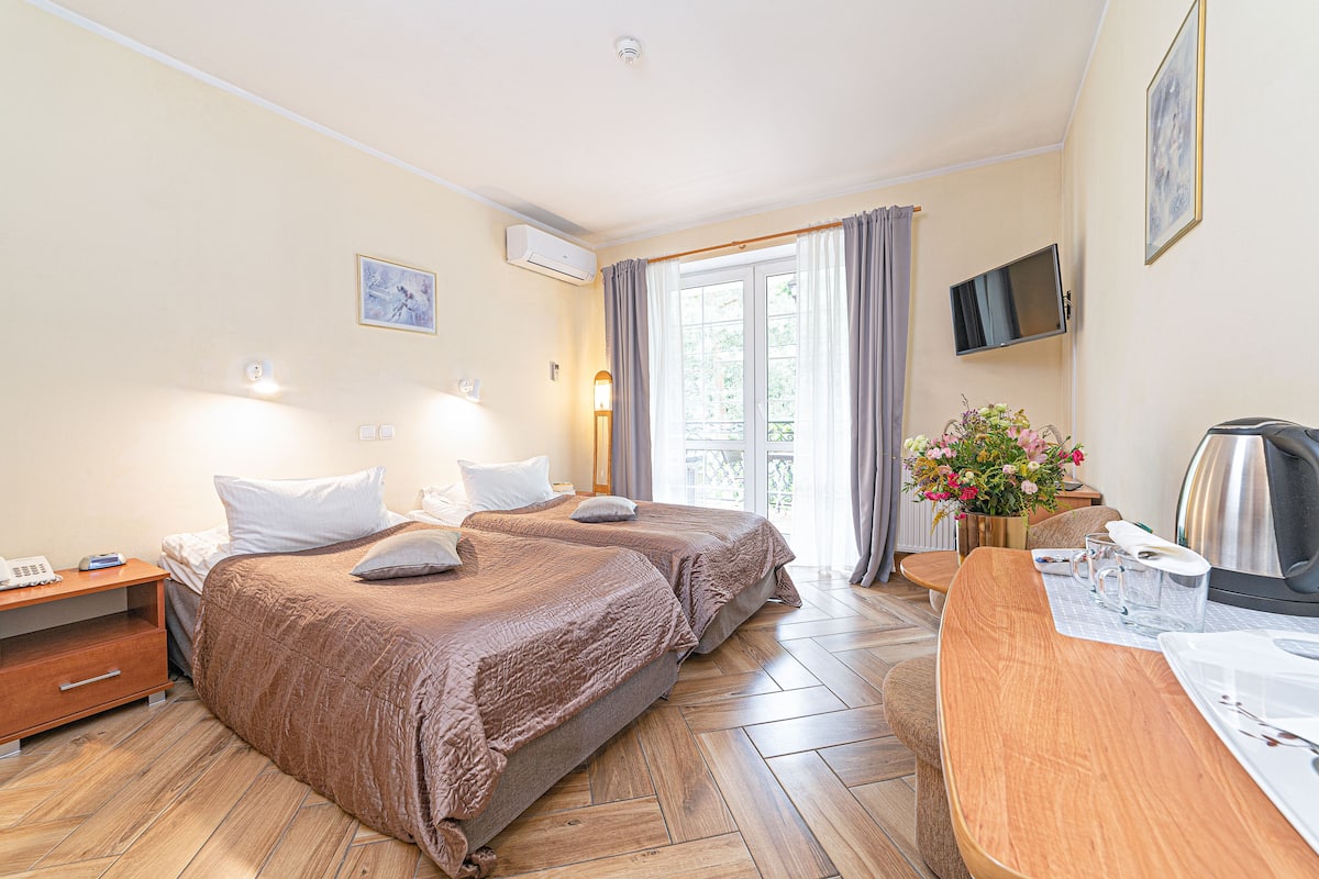 Habitación de hotel con dos camas, un escritorio con hervidor, televisor y ventana con cortinas.