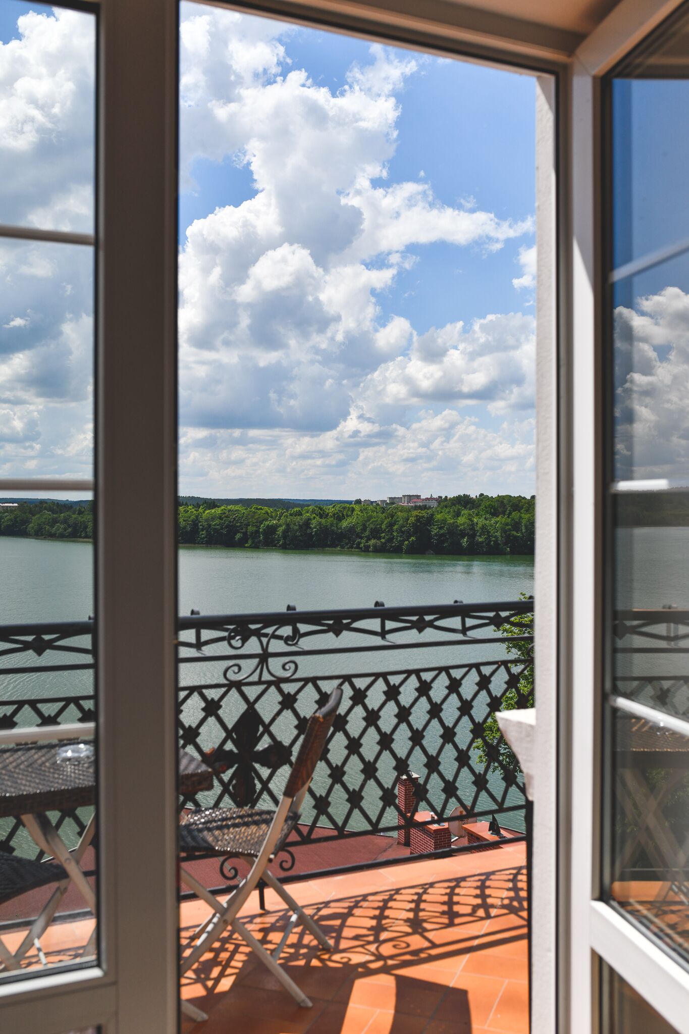 Ein Balkon mit Metallgeländer mit Blick auf einen See und einen bewaldeten Bereich.