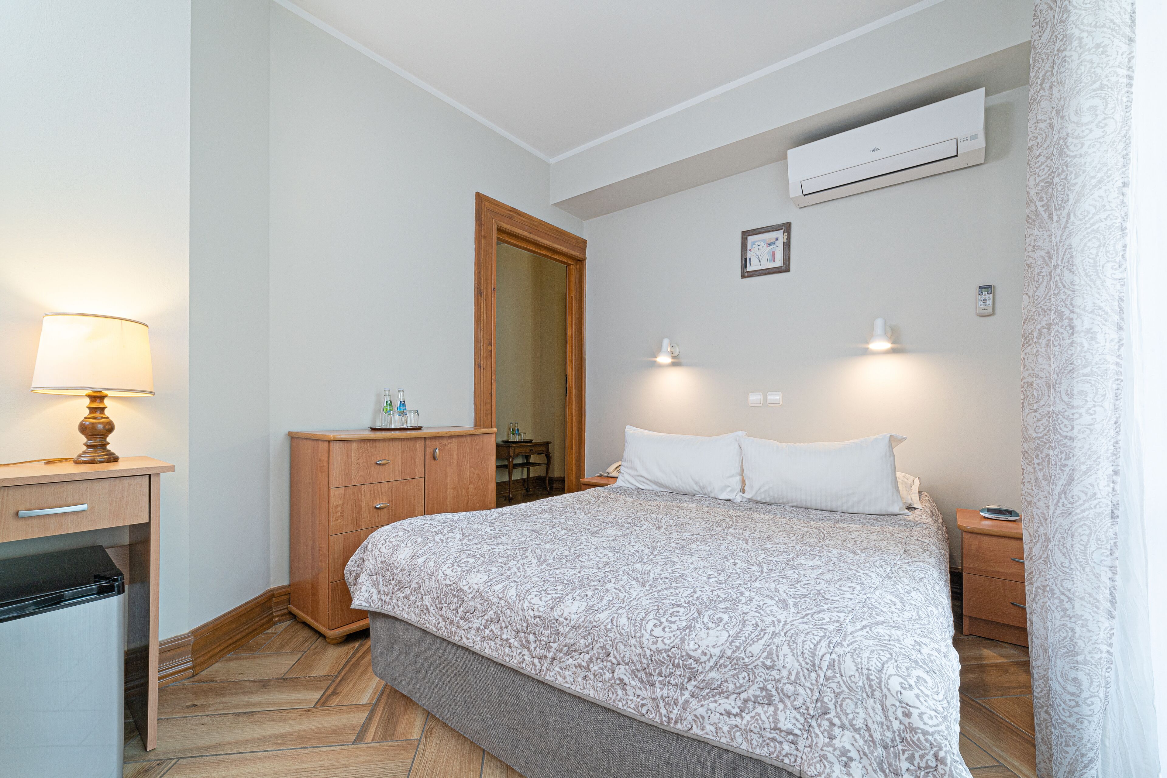 A bedroom with a bed, bedside tables, a desk, a wardrobe, and an air conditioning unit.