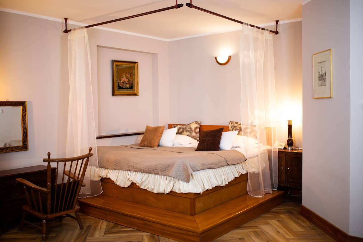 Un dormitorio con cama de madera, una silla, una mesita de noche, una lámpara y un cuadro en la pared.