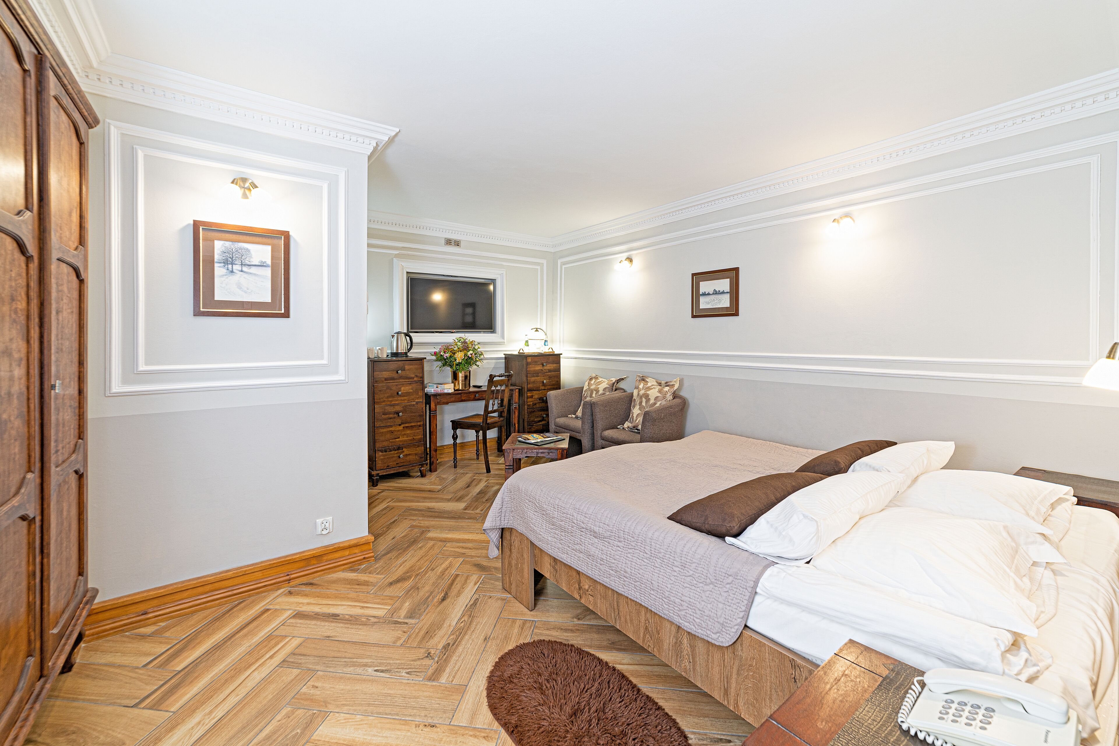 A hotel room with a bed, a desk, a TV, and a wooden wardrobe.