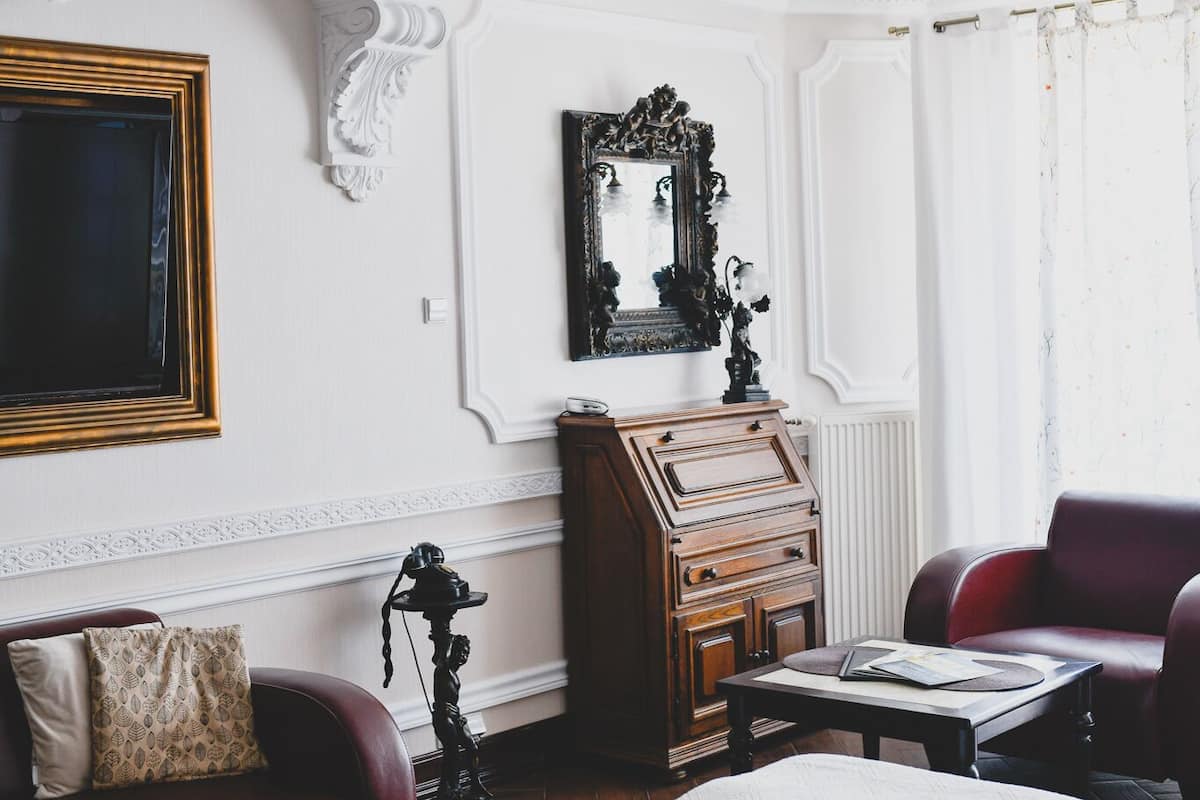 Una habitación con una cama, un aparador de madera, un sofá de cuero rojo, un candelabro y un espejo grande.