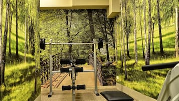A gym with a forest mural, weightlifting equipment, and a bench.
