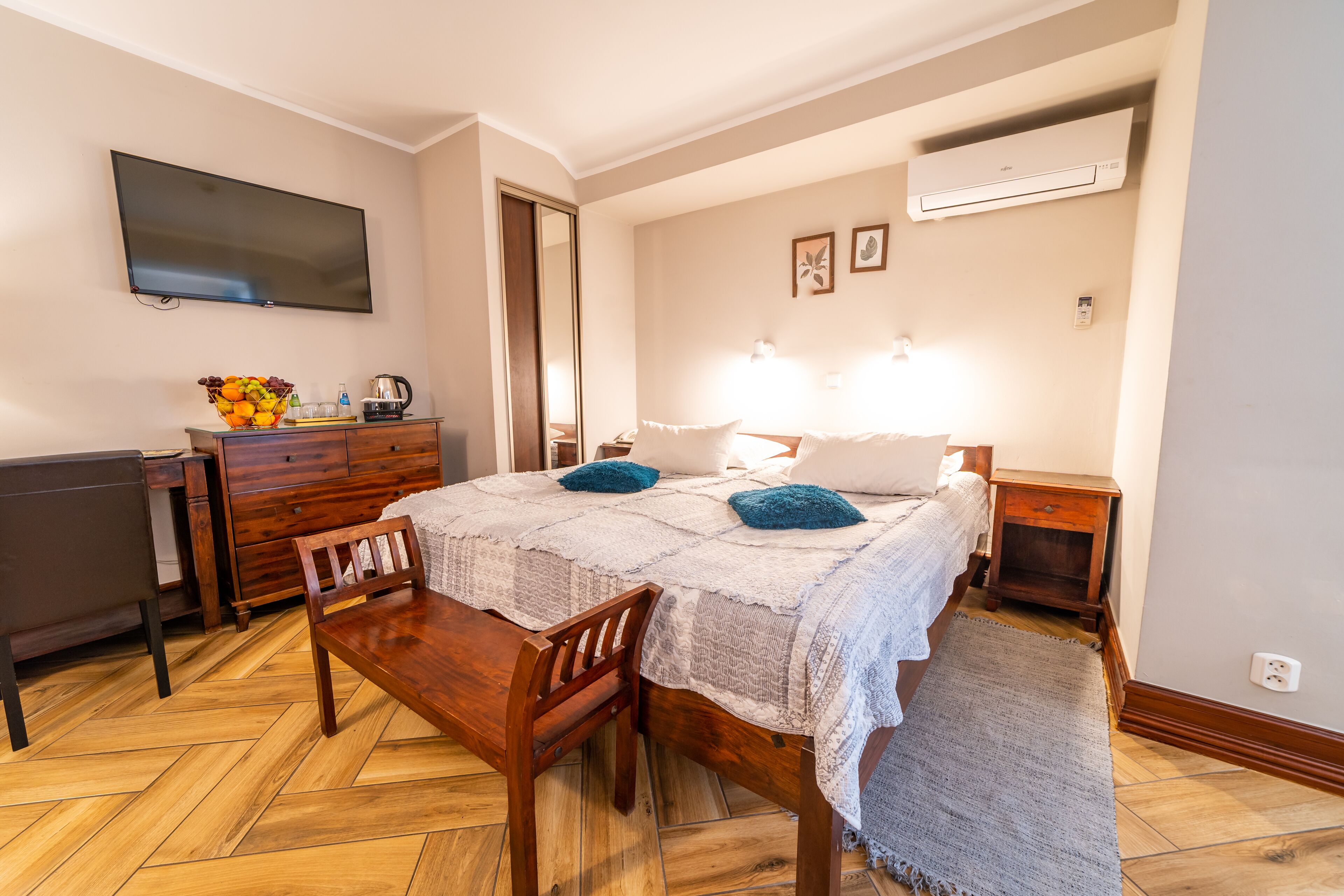 Un dormitorio con cama, mesitas de noche, escritorio, silla, televisor y frutero.