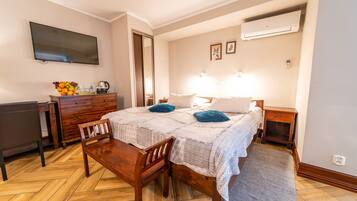 Une chambre à coucher comprenant un lit, des tables de chevet, un bureau, une chaise, une télévision et un panier de fruits.