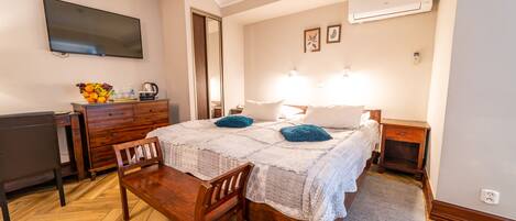 A bedroom with a bed, bedside tables, a desk, a chair, a TV, and a fruit bowl.