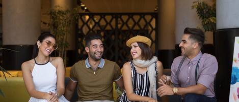 A group of people sitting on a yellow couch in a lobby with a geometric wall design and plants.