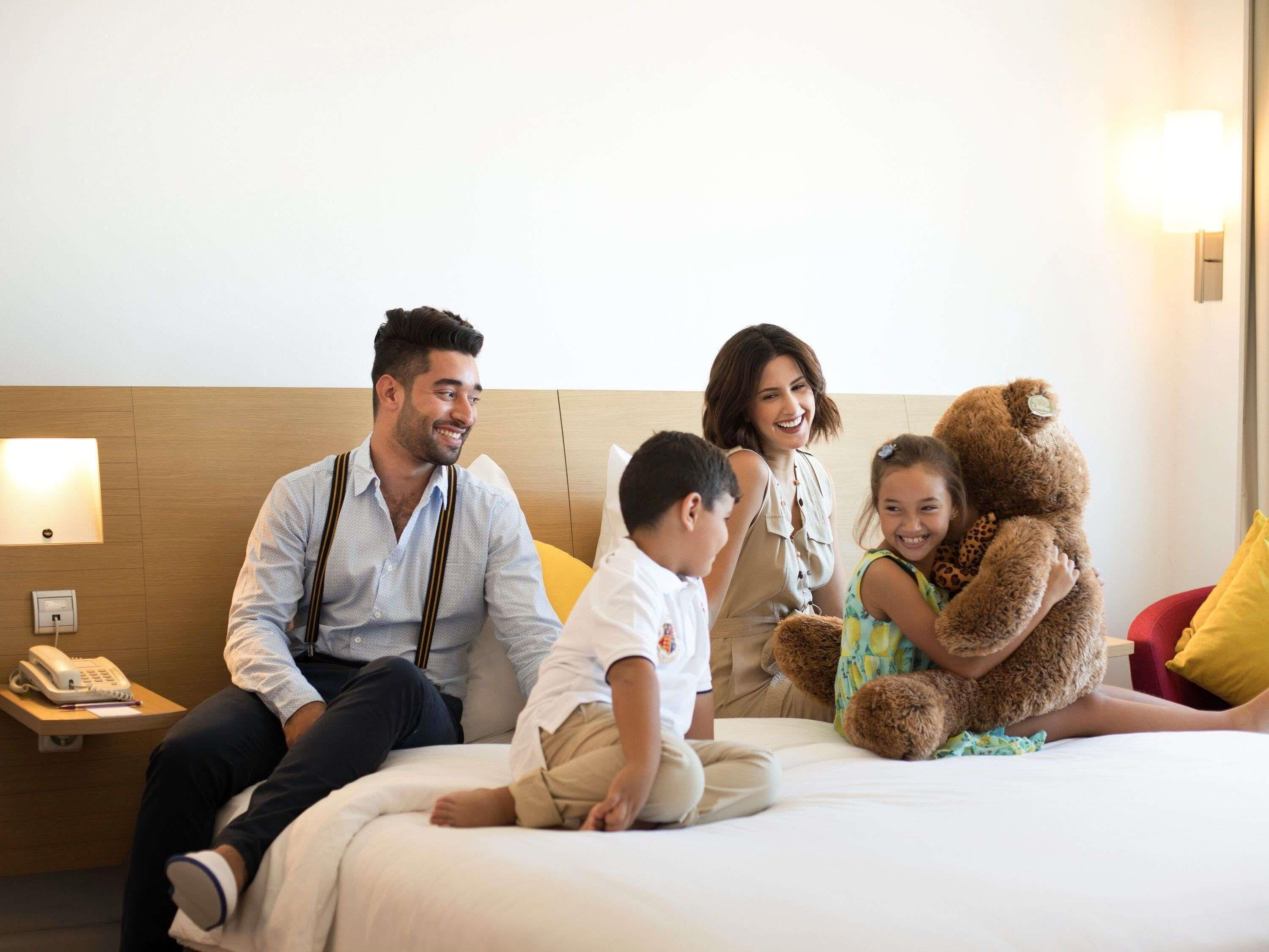 Una habitación de hotel con una cama, una mesita de noche con un teléfono y una lámpara fijada a la pared.