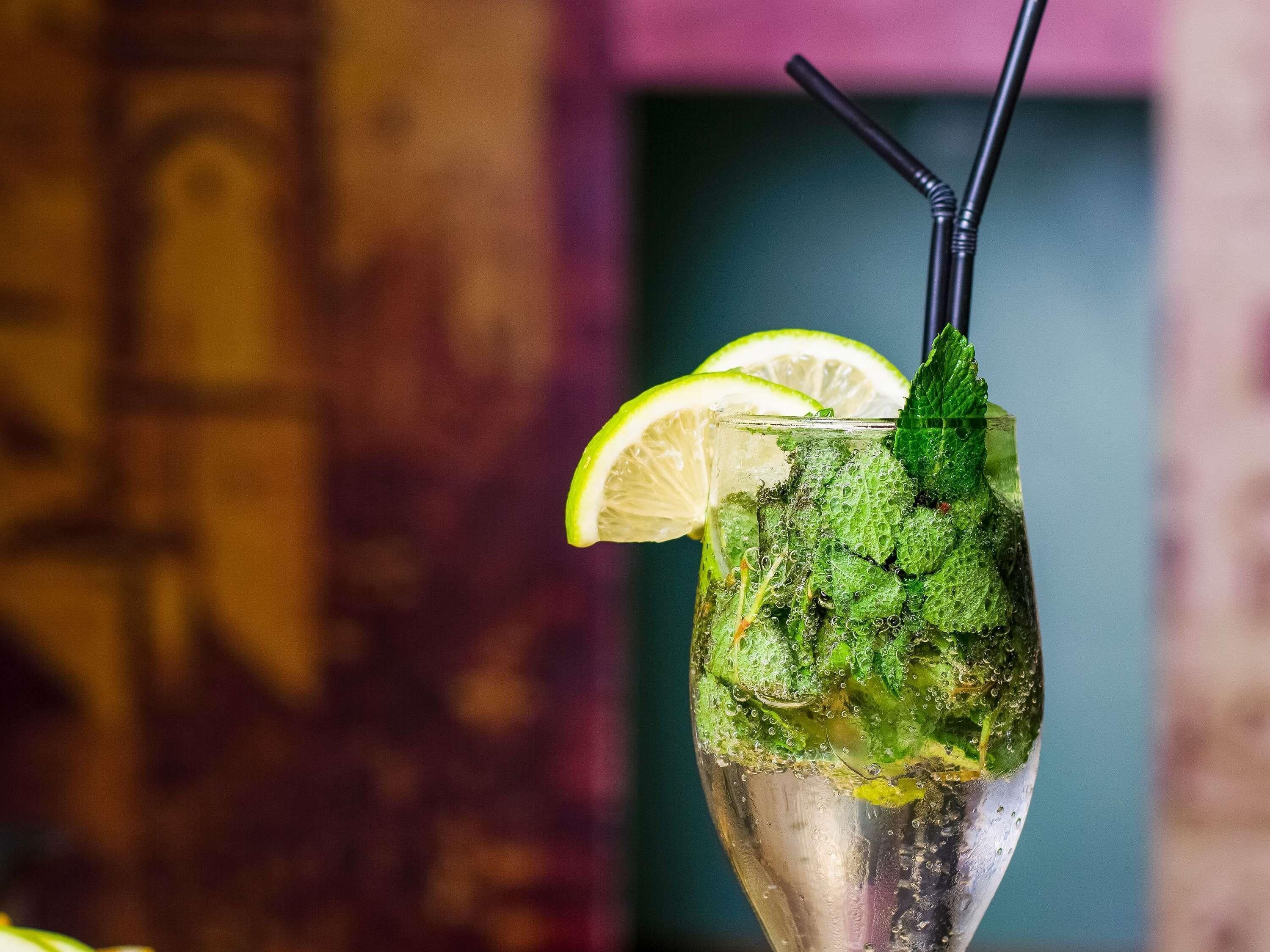A glass with a lime slice, mint leaves, and a straw.