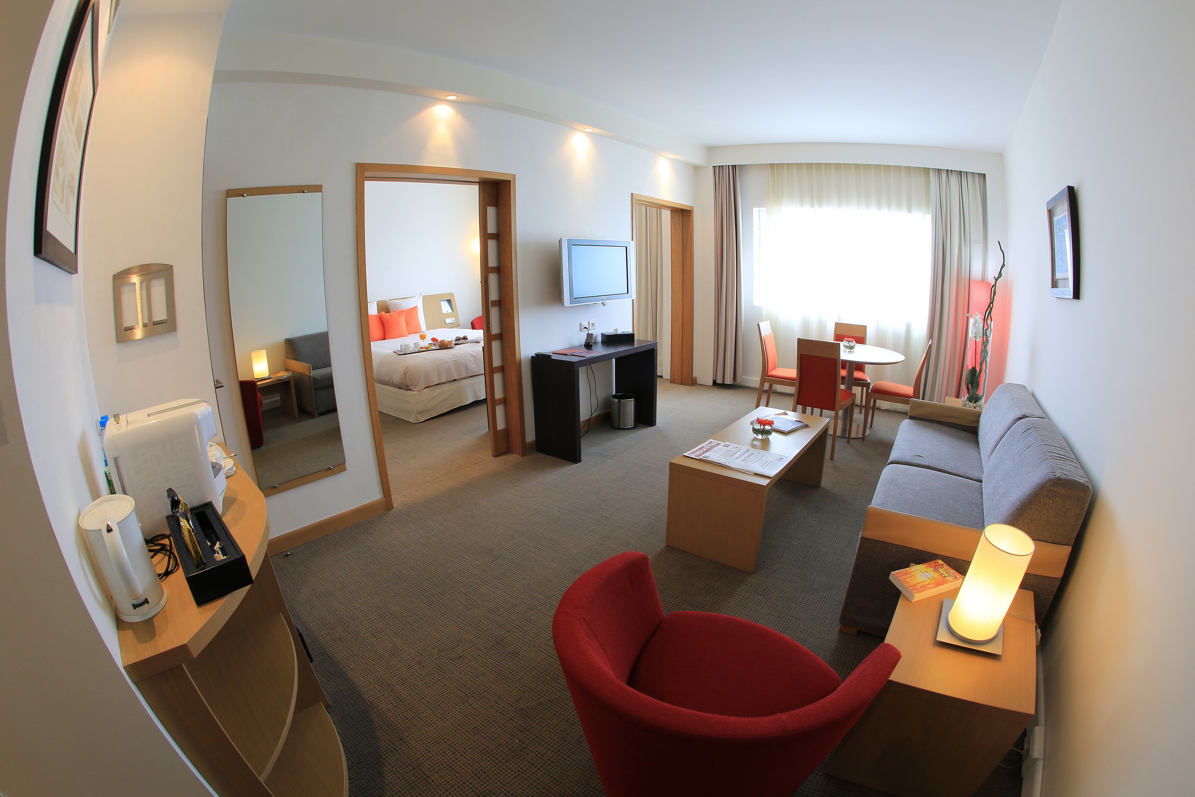 Hotelkamer met een zithoek, televisie, bureau, rode stoel, bank en een eettafel.