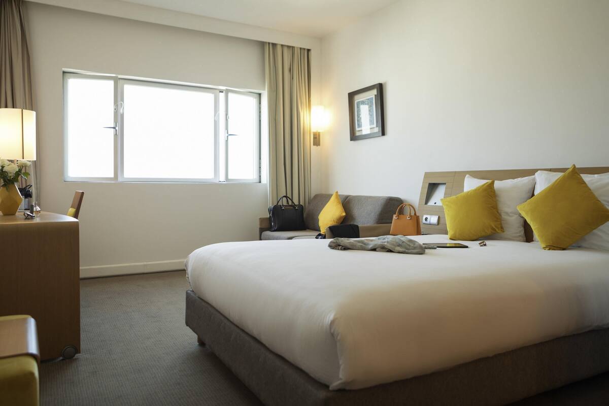 Une chambre d’hôtel avec un grand lit, une table de chevet, une lampe, une fenêtre et un tableau au mur.