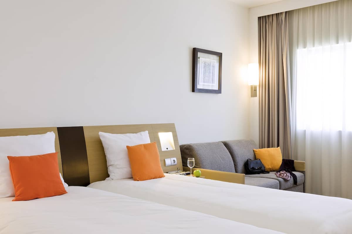 A hotel room with two beds, a sofa, a framed picture on the wall, and a window with curtains.