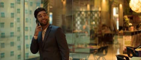 Un hombre con traje habla por teléfono dentro de un edificio moderno con paredes de vidrio, un comedor y una araña.