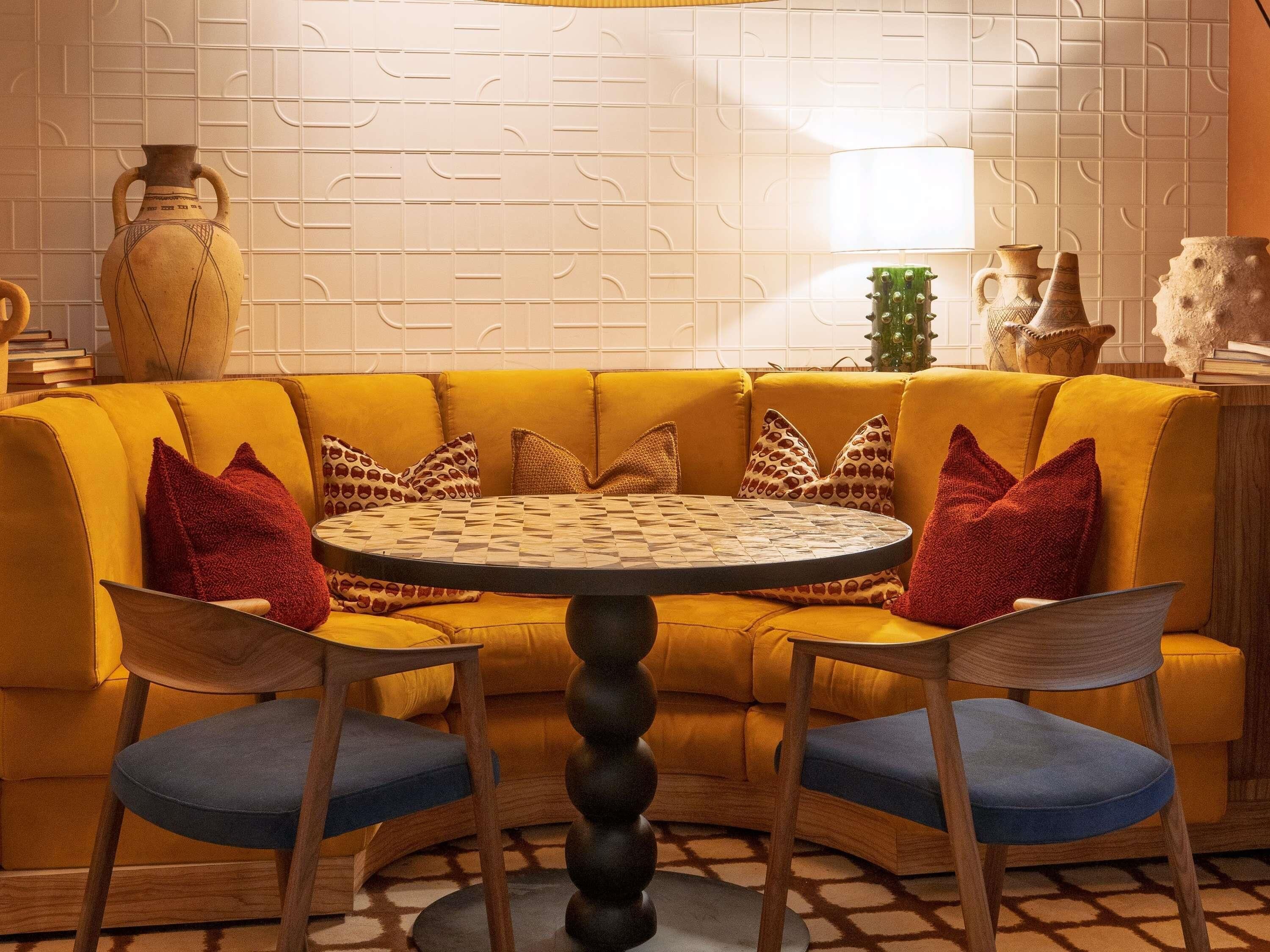 A yellow sofa with blue chairs, a round table, and decorative vases.