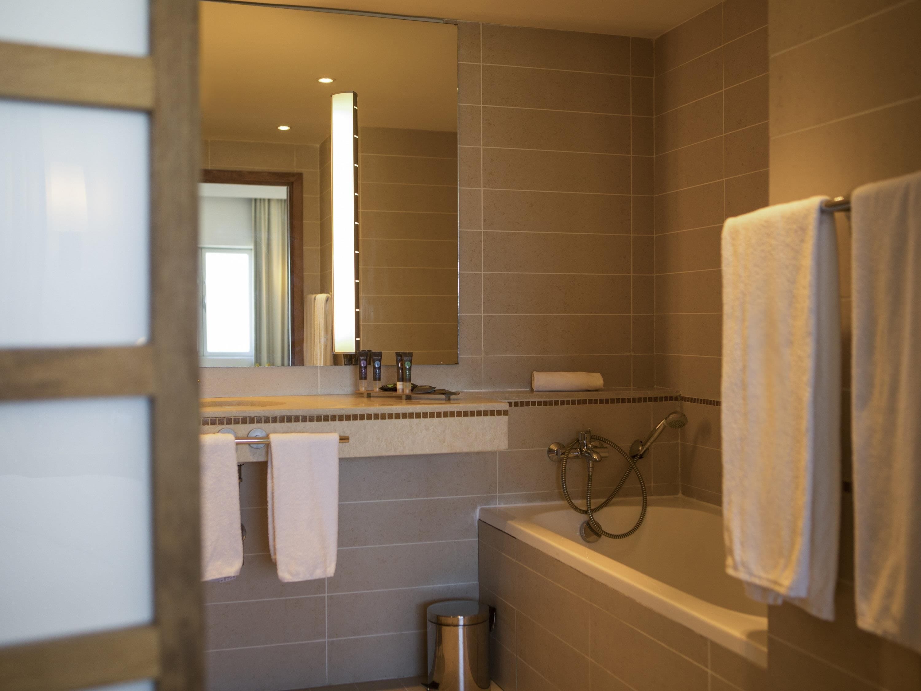 Un baño moderno con bañera, ducha y tocador con espejo. Hay toallas colgadas en la pared y un cubo de basura.