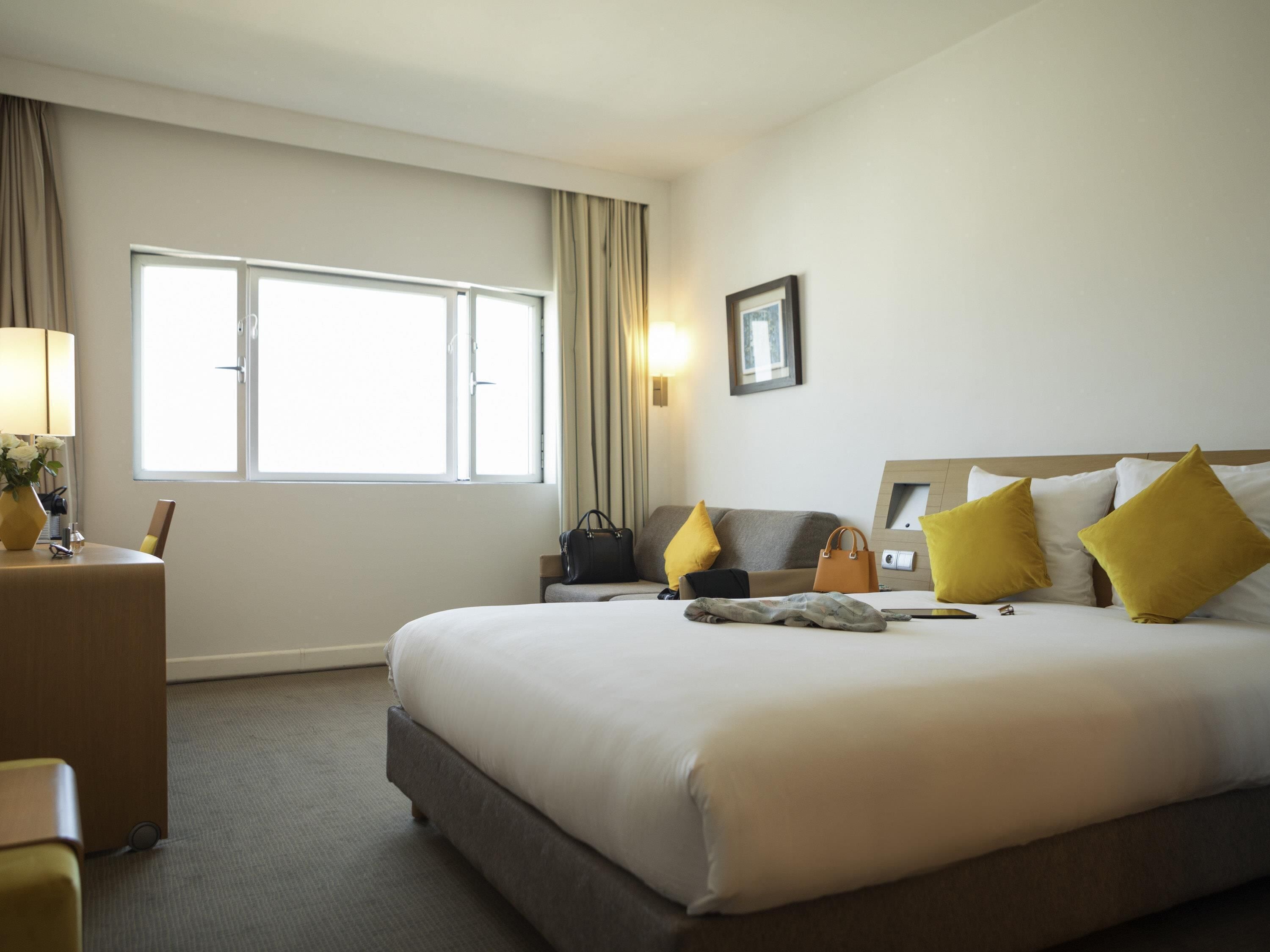 A hotel room with a large bed, a bedside table, a lamp, a window, and a picture on the wall.