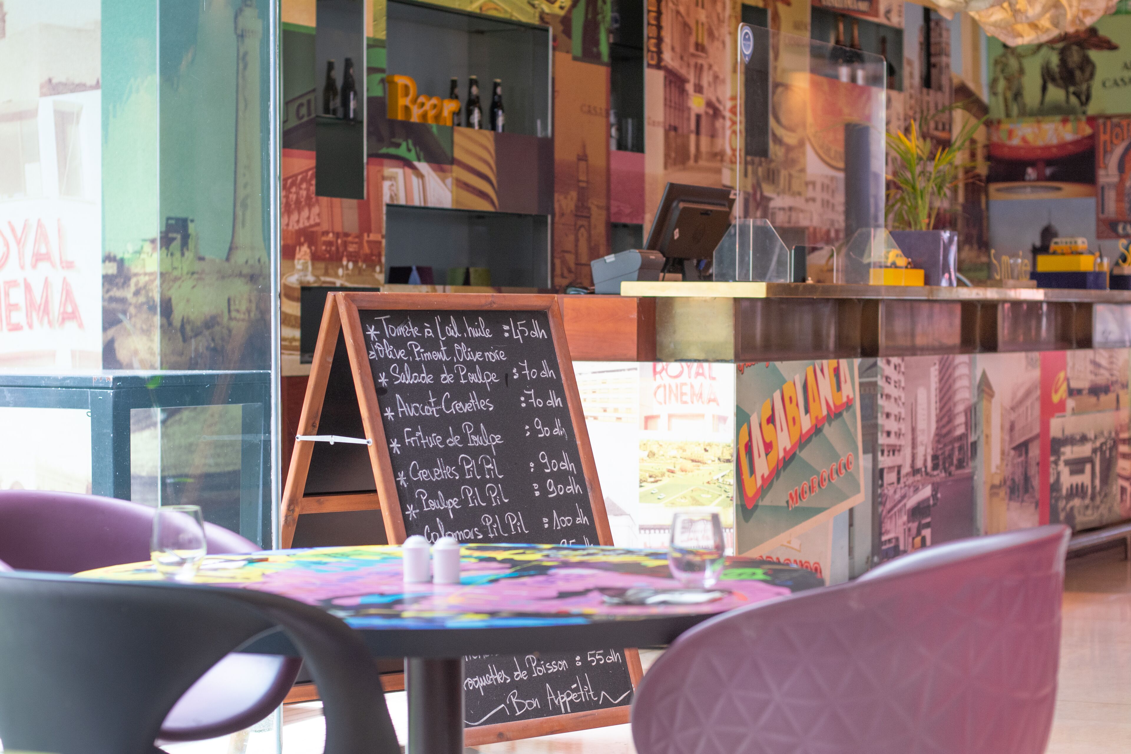 Een restaurant interieur met een krijtbordmenu, kleurrijke decoratie en uitzicht op het terras.
