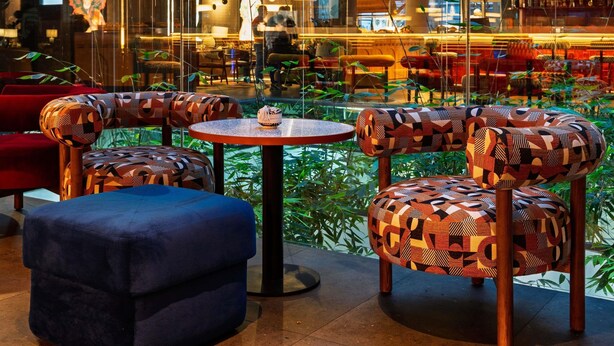 A modern interior with geometric patterned furniture, a central round table, and a view of a restaurant area. - Novotel Casablanca City Center (Casablanca)