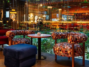 Un interior moderno con mobiliario de diseño geométrico, una mesa redonda central y vista a un área de restaurante.