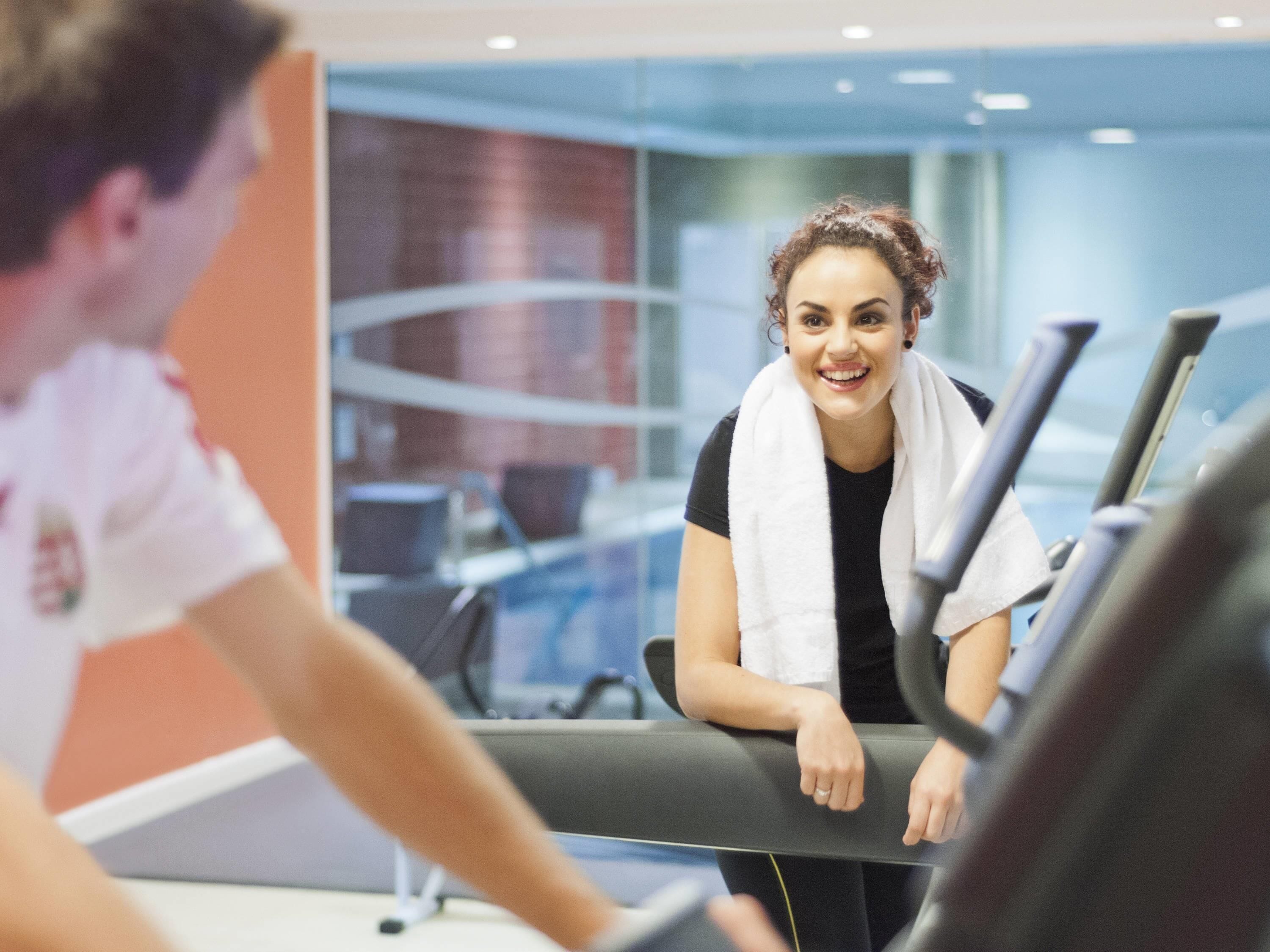 A person using a treadmill in a gym with a glass wall and a red wall in the background.
