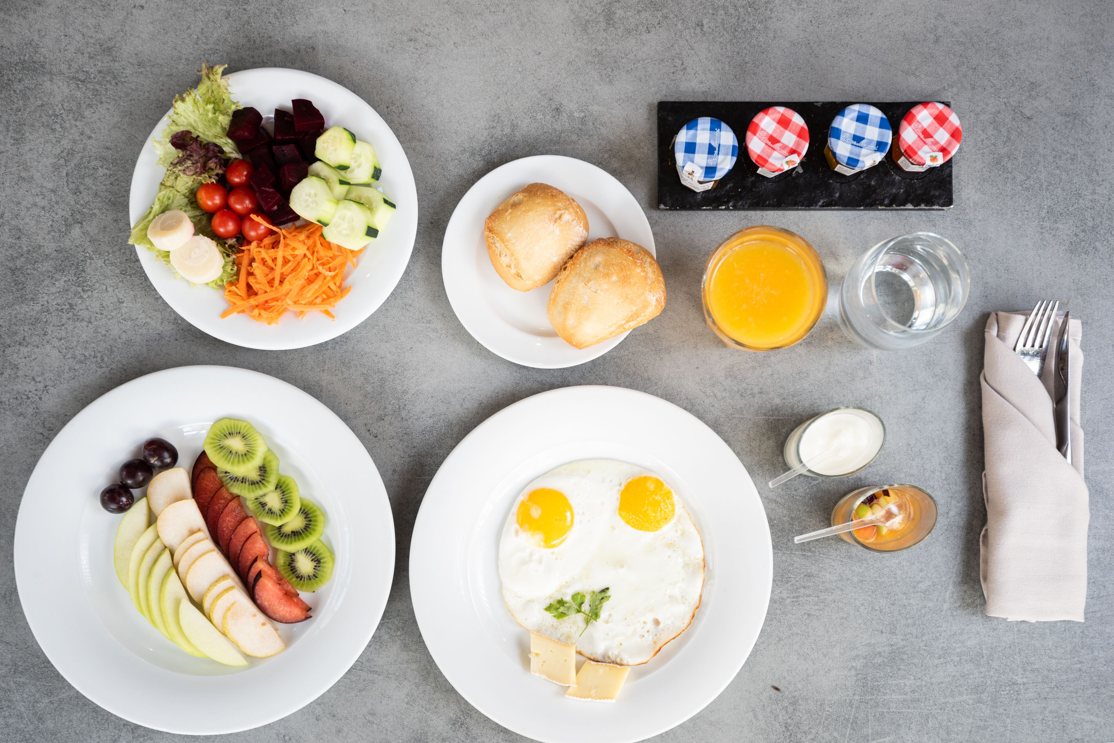 A breakfast setting with plates of food, a napkin, and a glass of orange juice.