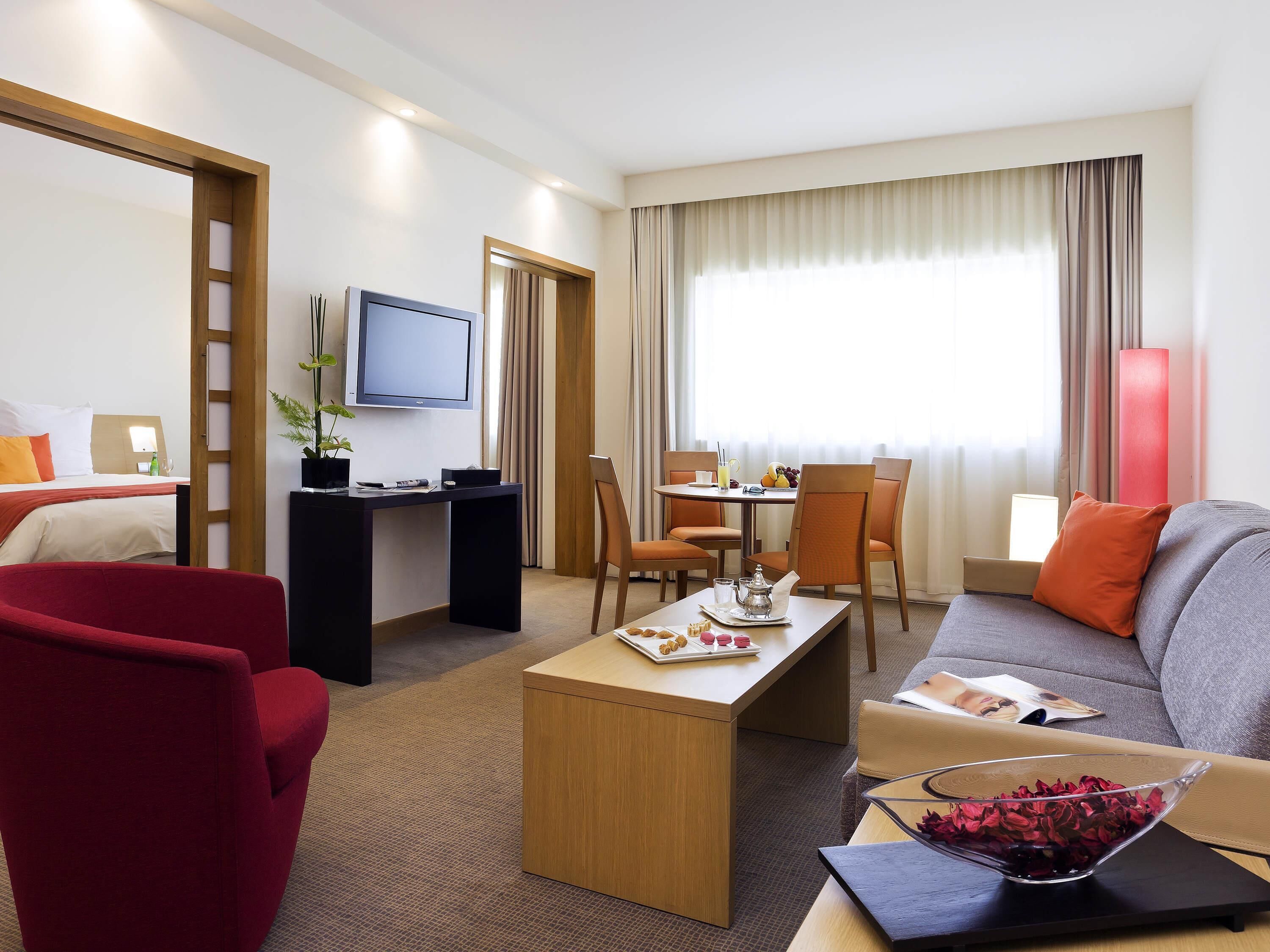 Habitación de hotel con cama, escritorio, televisor, zona de comedor y sofá.