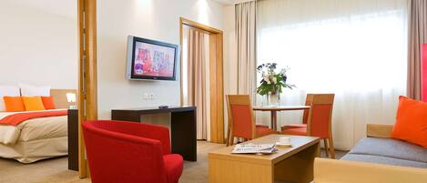 Una habitación de hotel con cama, televisión, escritorio, mesa de centro y dos sillas.