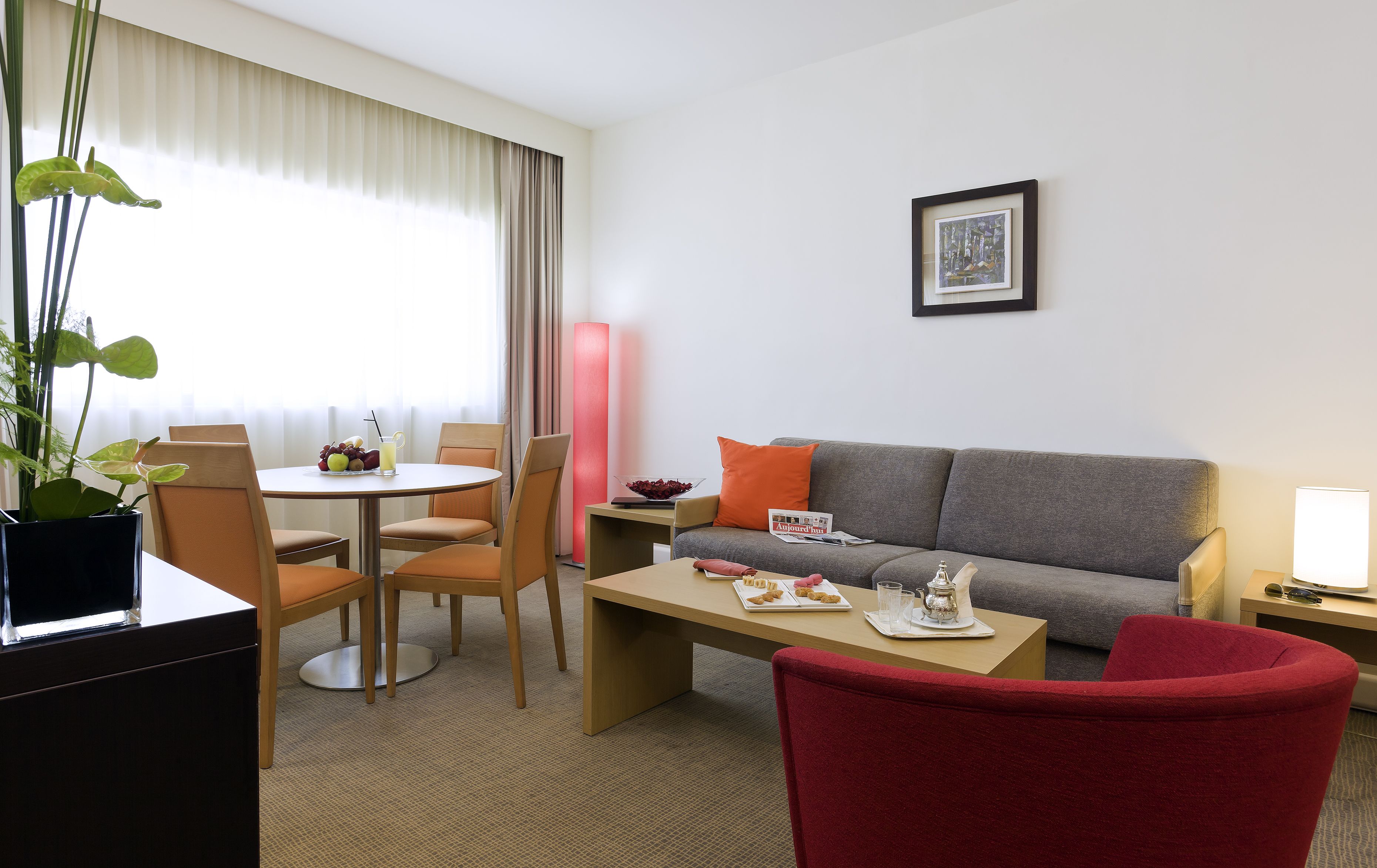 Une chambre d’hôtel avec un coin repas, un canapé et un fauteuil rouge.