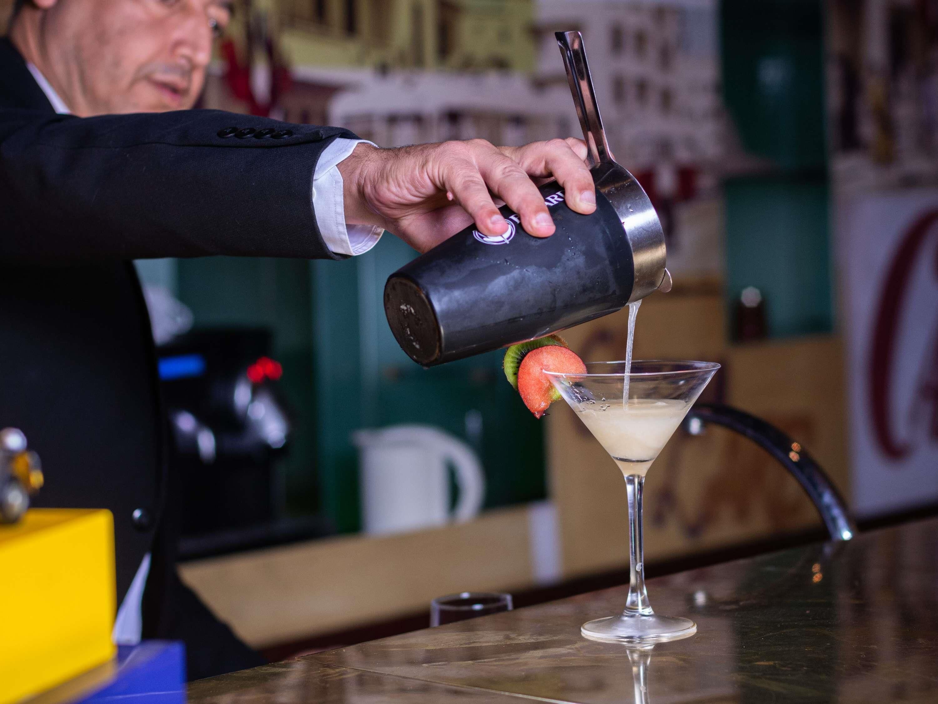 Een barman giet een drankje in een martini-glas.