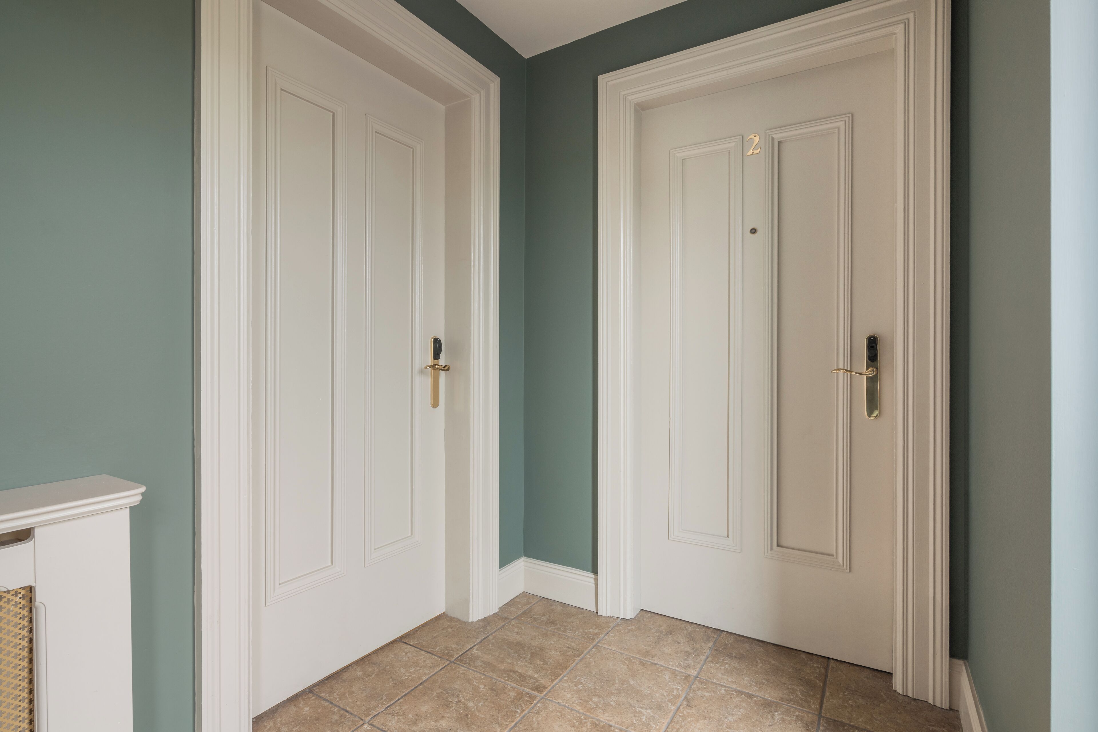A hallway with two white doors, a white fireplace, and beige tiled flooring.