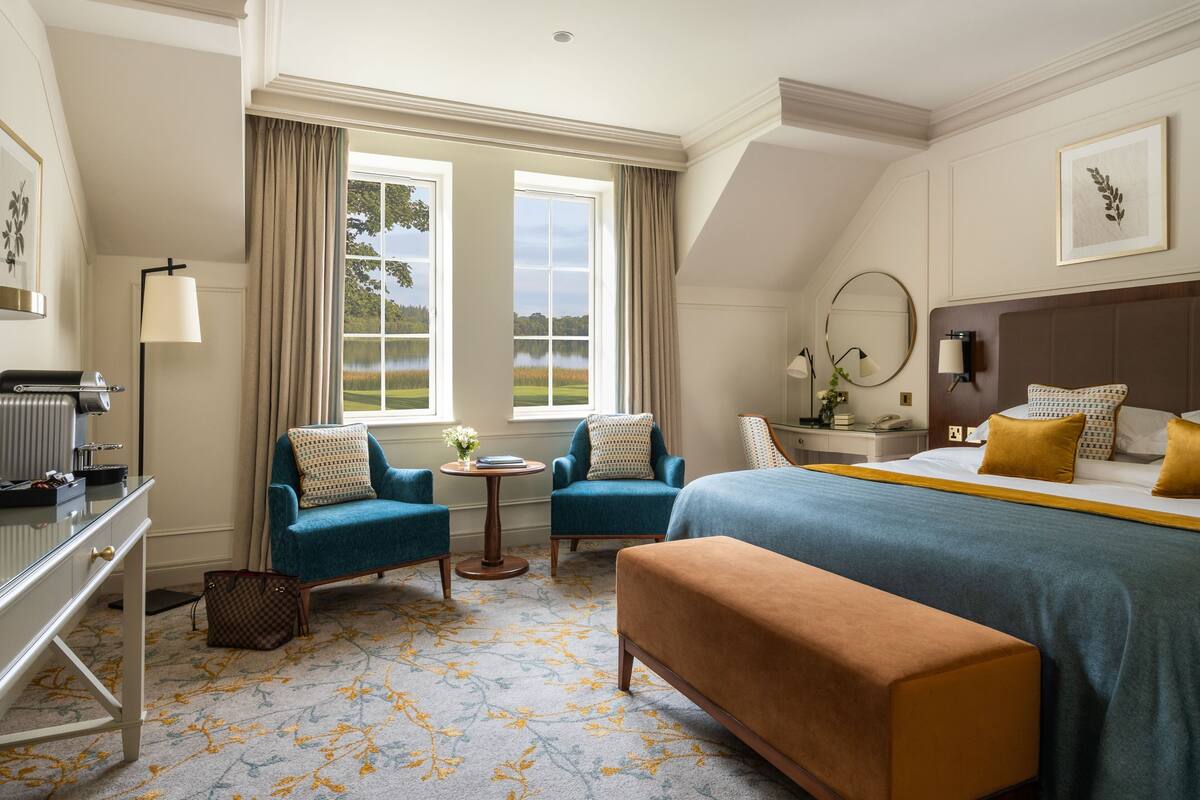 A hotel room with a large bed, two armchairs, a desk, and a view of a lake.