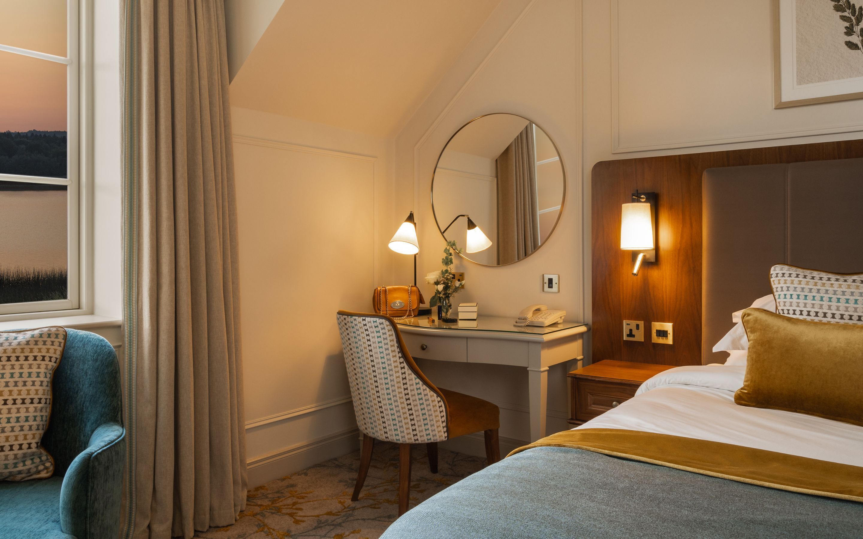 A hotel room with a bed, a desk, a chair, a mirror, and a window with curtains.