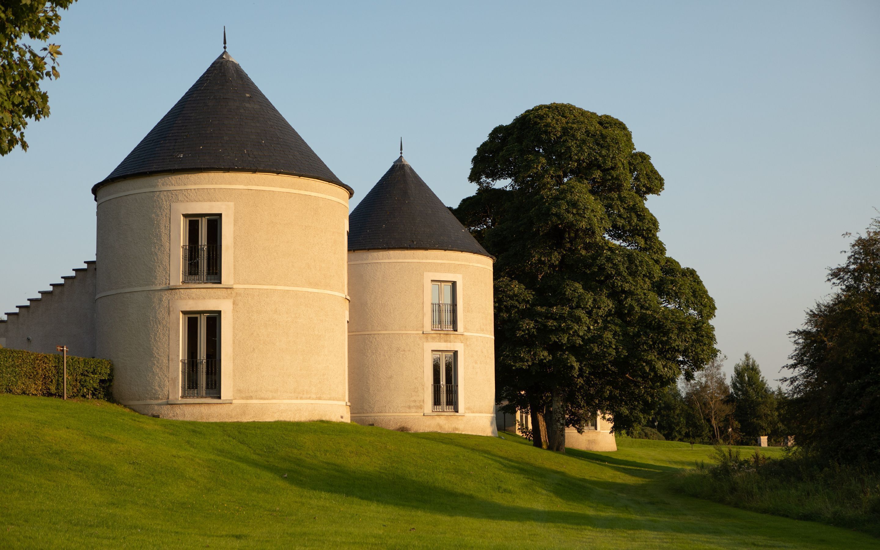 Un bâtiment cylindrique à deux étages, surmonté d’un toit conique, entouré d’une pelouse bien entretenue et d’un grand arbre.