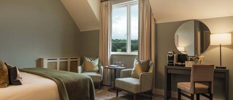 A bedroom with a bed, two armchairs, a desk, a mirror, and a window with curtains.