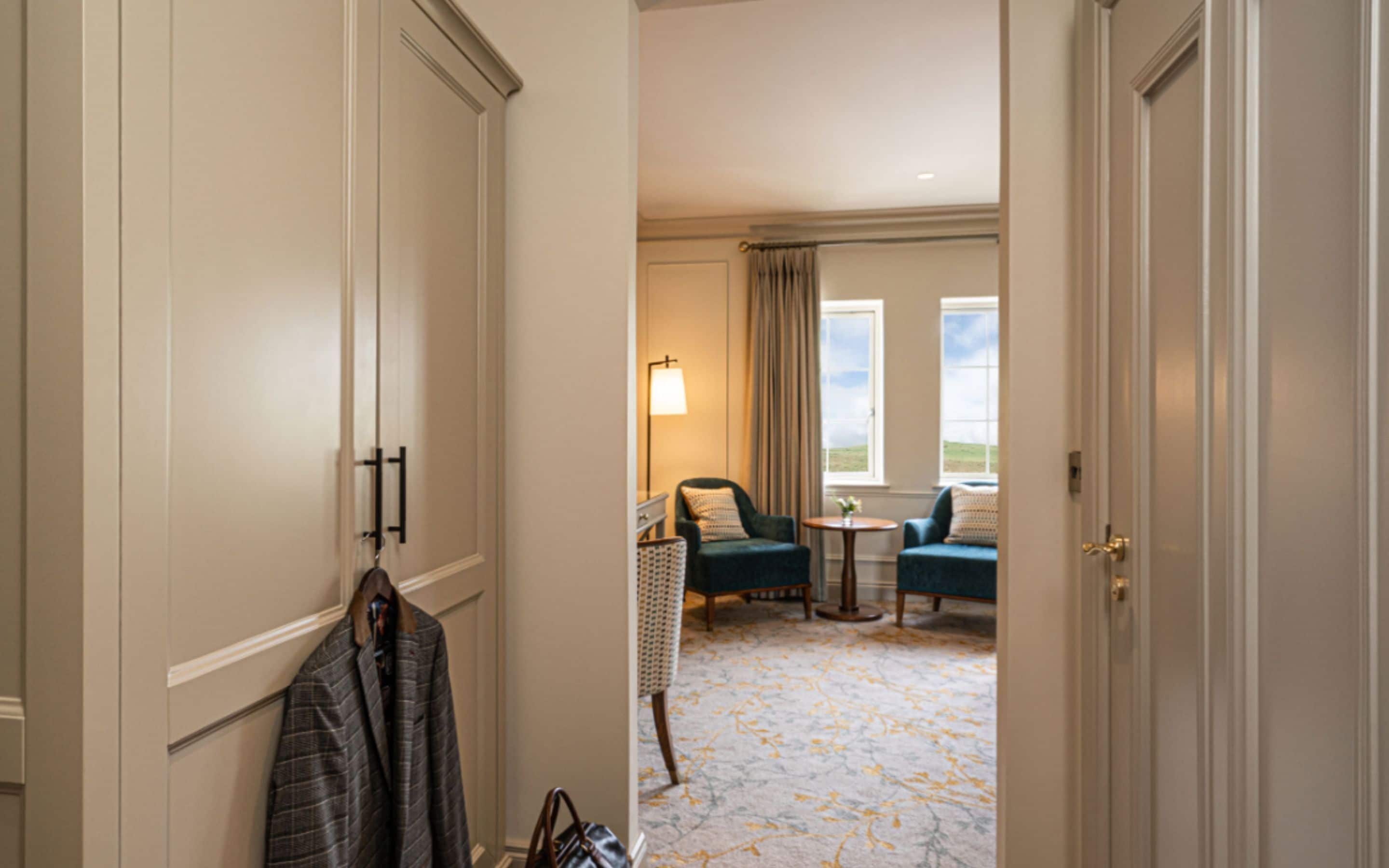 Ein Hotelzimmer mit großem Kleiderschrank, einer Sitzecke inklusive Tisch und Stühlen sowie Blick ins Freie durch ein Fenster.