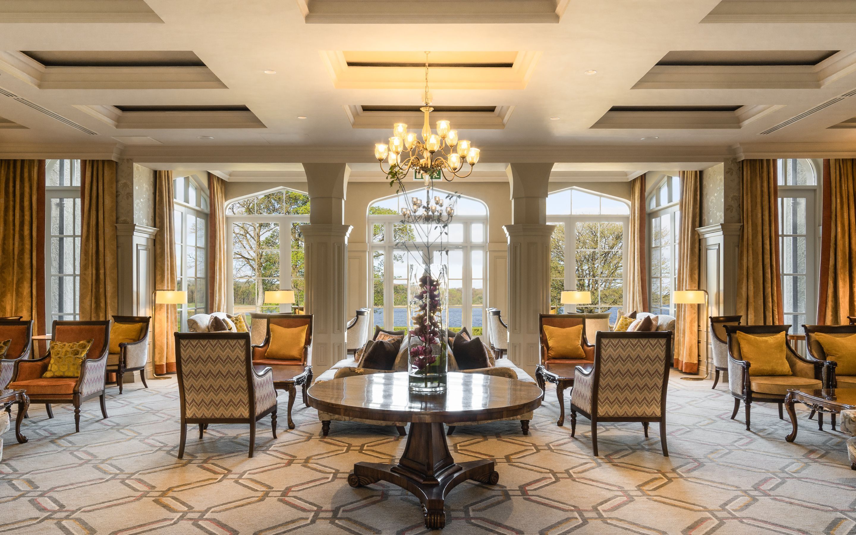 Une pièce spacieuse avec une grande table ronde entourée de chaises, de grandes fenêtres avec des rideaux et un lustre.