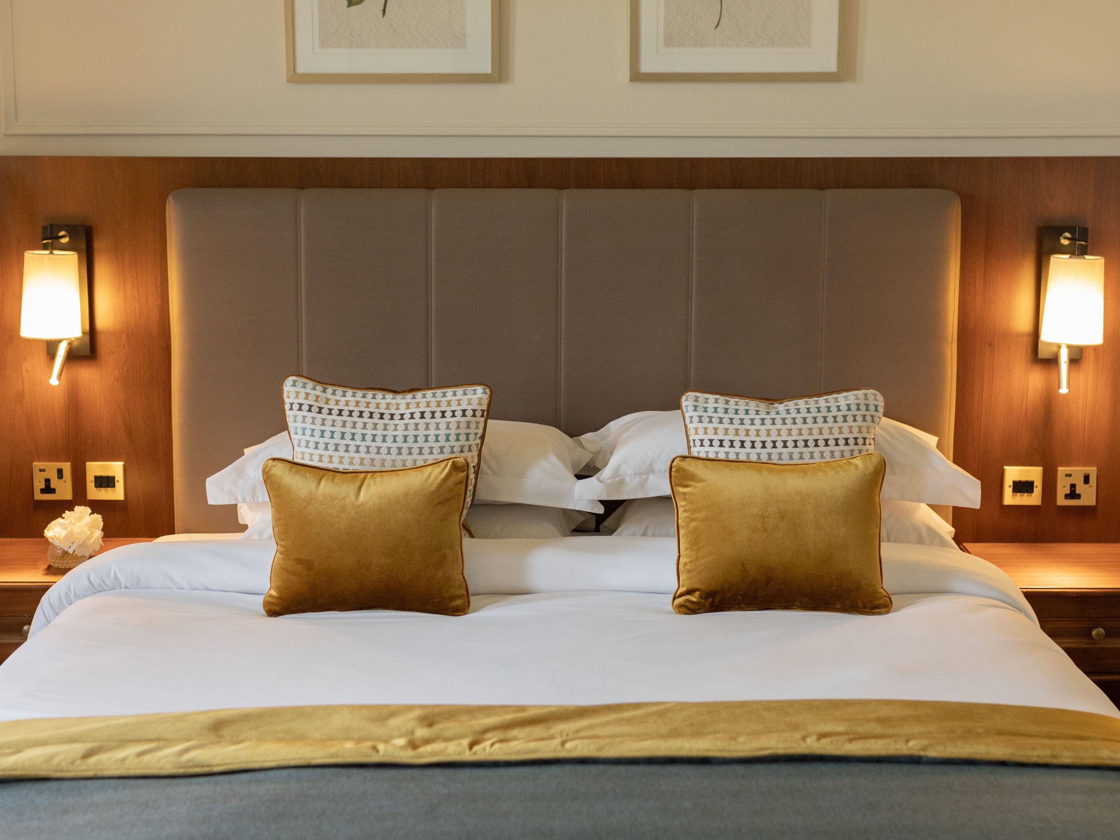 A neatly made bed with two patterned pillows and two solid-colored pillows, flanked by wall-mounted lamps.