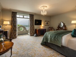 Una habitación de hotel con una cama grande, un escritorio con lámpara, una silla, un aparador, un espejo y un balcón con cortinas.