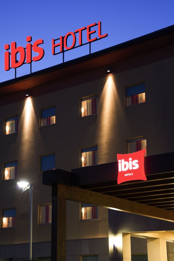 Un hotel con un llamativo letrero que dice 'ibis HOTEL', múltiples ventanas y un área de acceso cubierta.