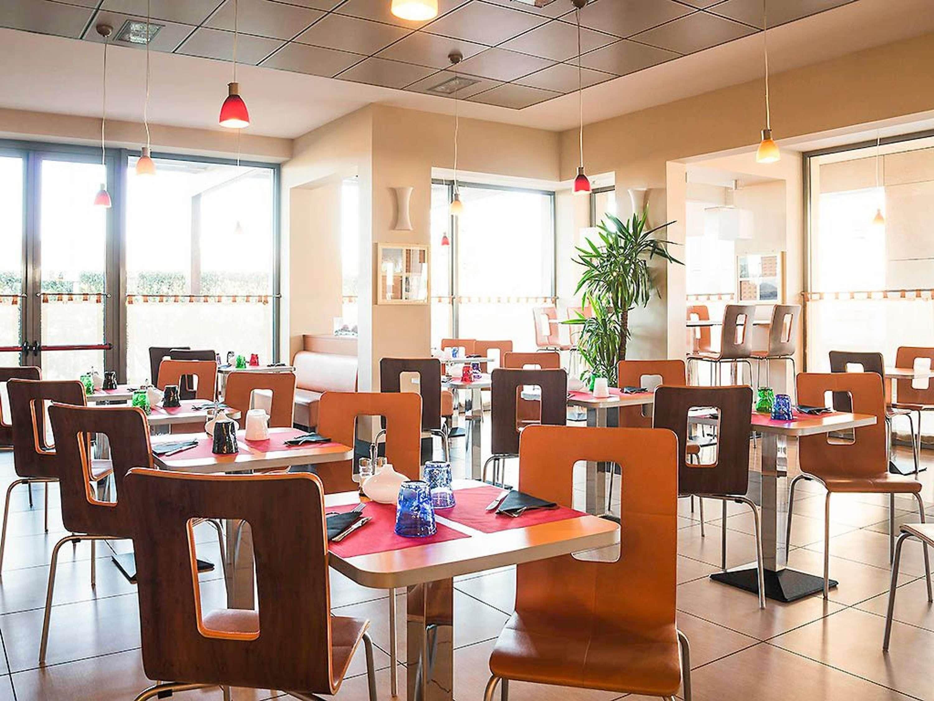A restaurant with multiple tables and chairs, large windows, and hanging pendant lights.