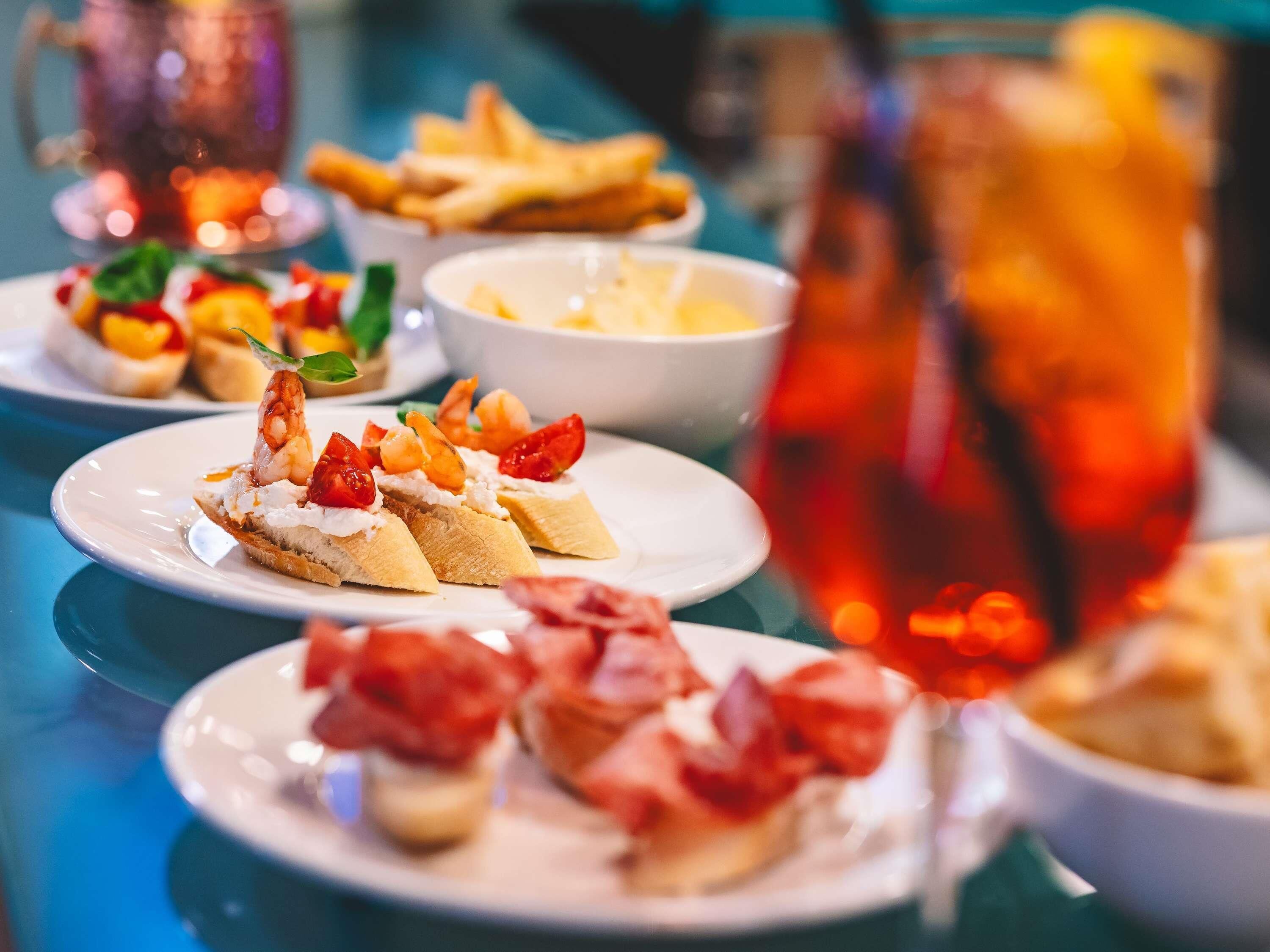 A table with various dishes, including shrimp and tomato-topped bread, and a glass of iced beverage.