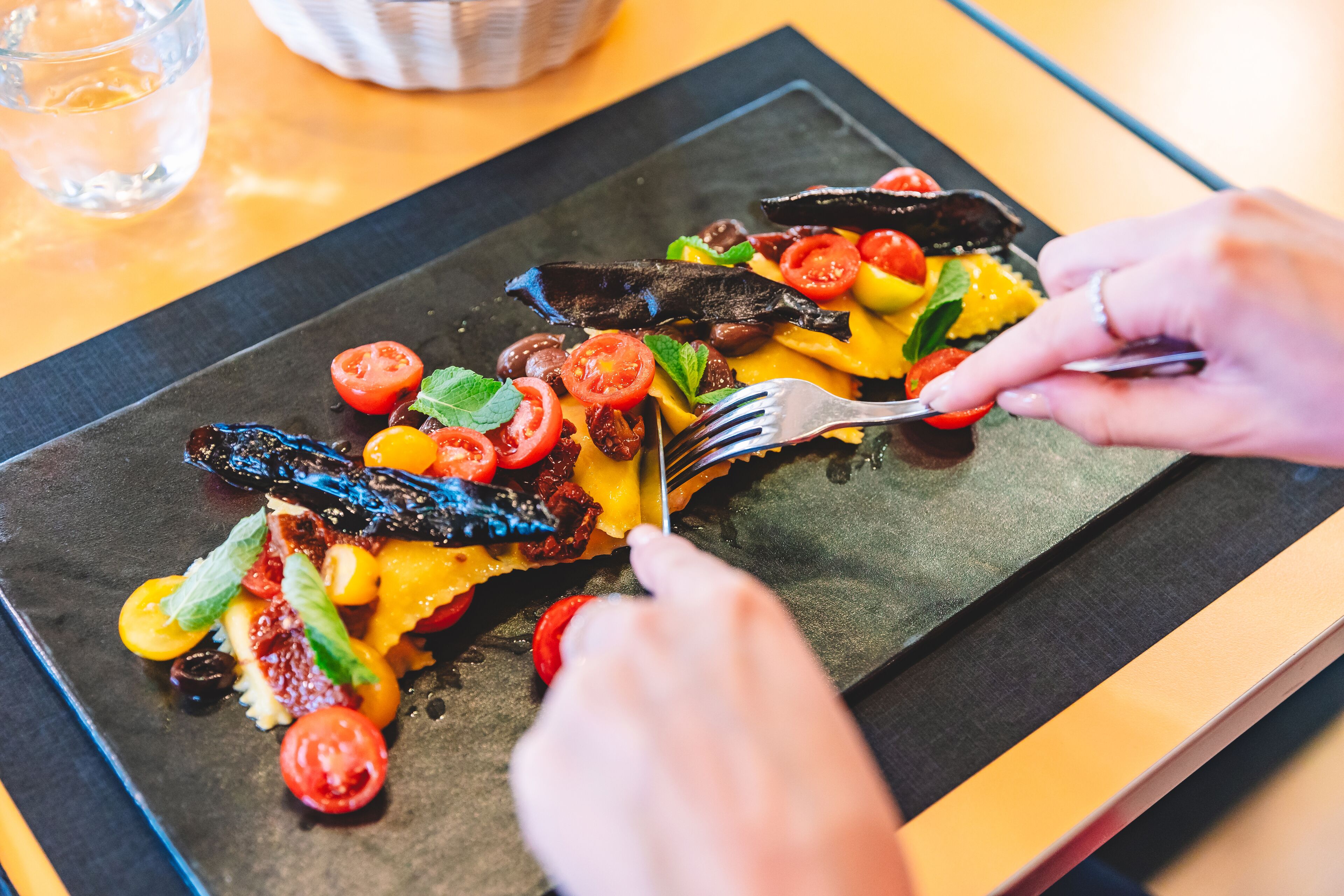 A person cutting a dish with various vegetables and cheese on a black plate.
