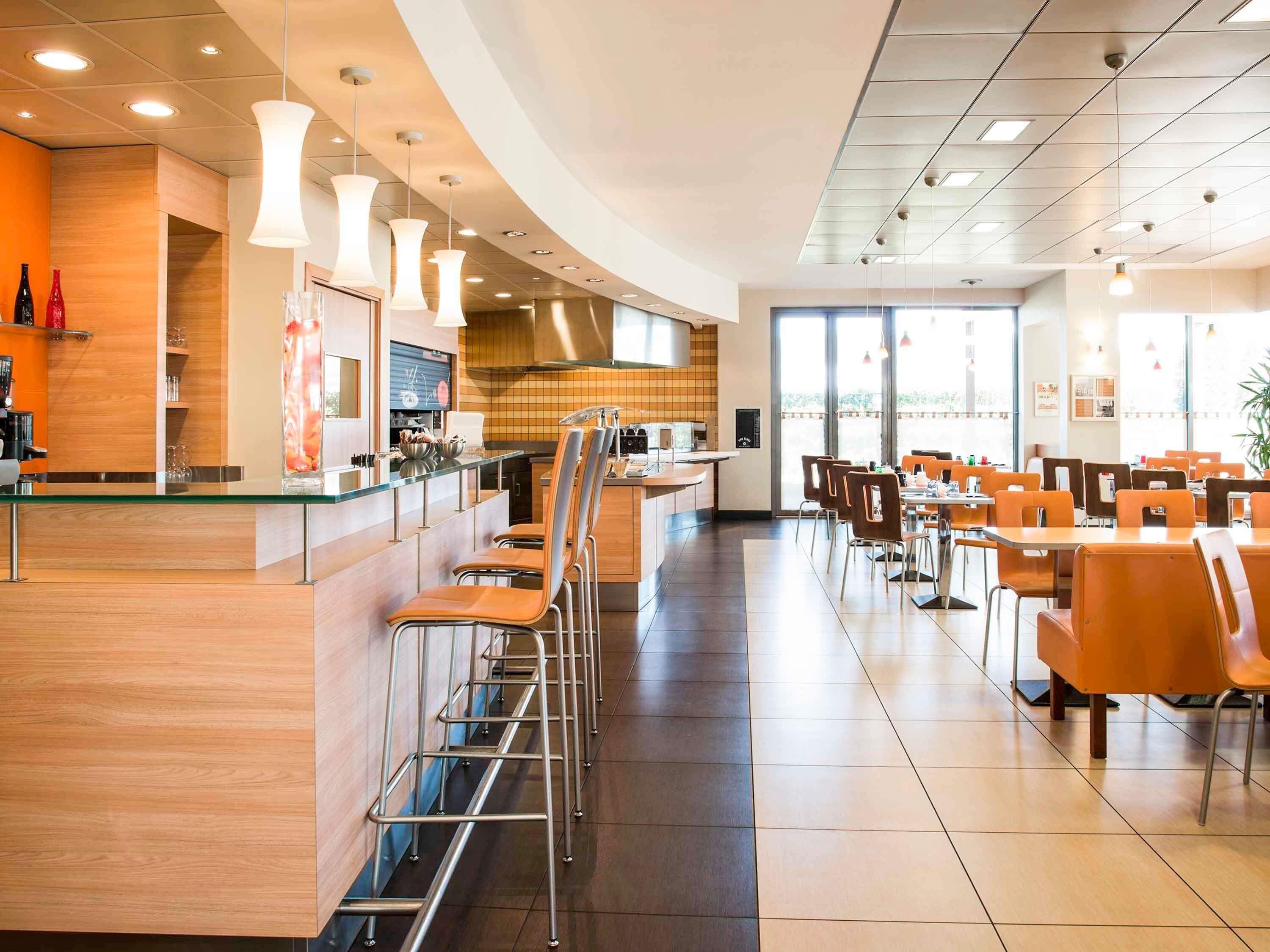Un interno ristorante moderno con zona bar, posti a sedere e cucina sullo sfondo.