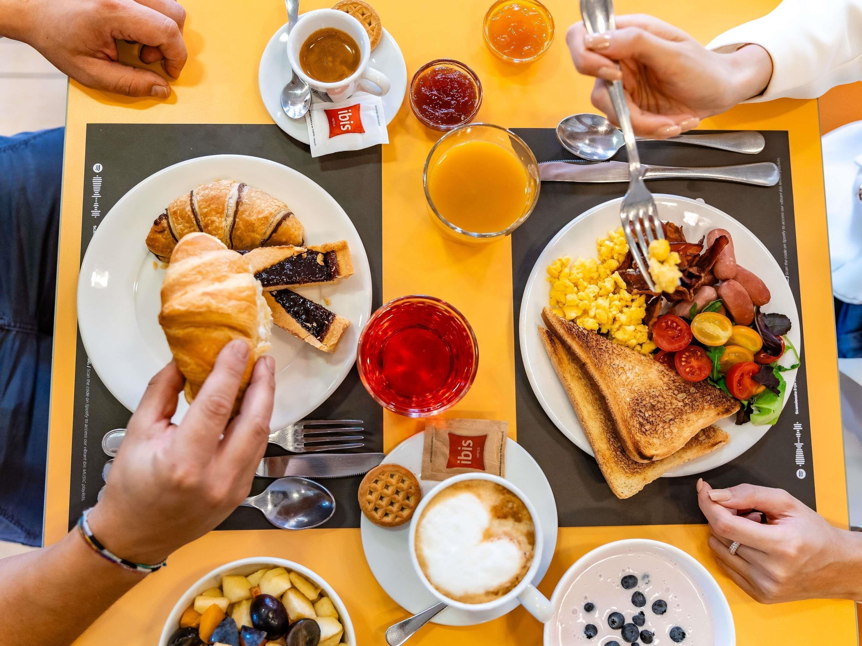 A breakfast setting with croissants, toast, scrambled eggs, bacon, tomatoes, and a cup of coffee.