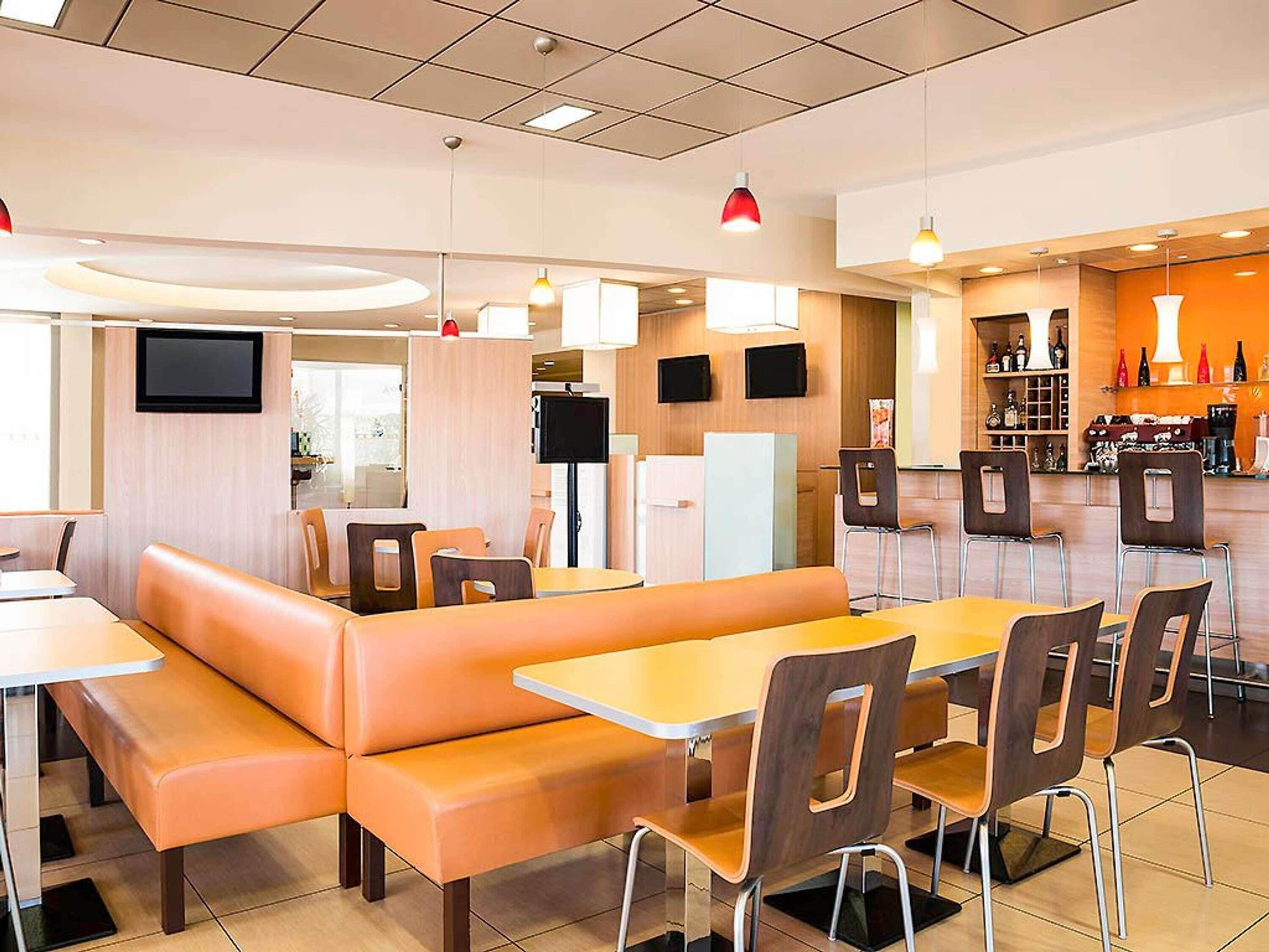A modern restaurant with booths and tables, a bar area, and a flat-screen TV.