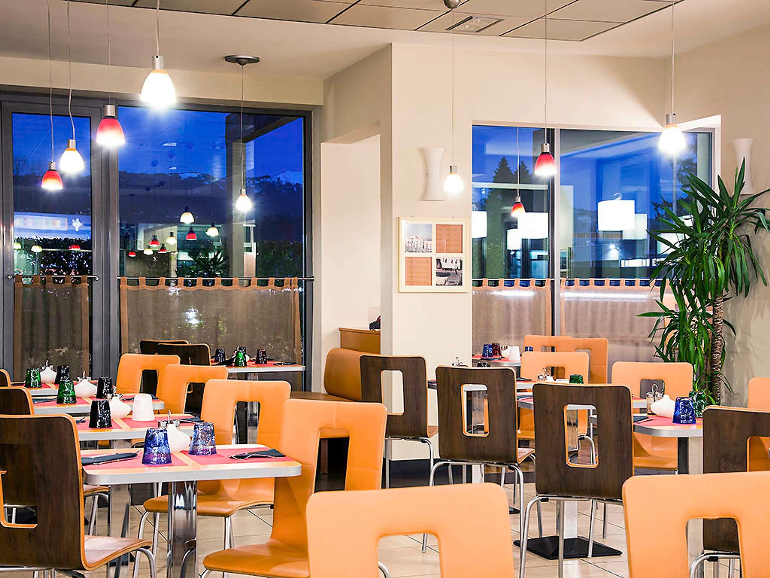 A restaurant with tables and chairs, large windows, and hanging lights.