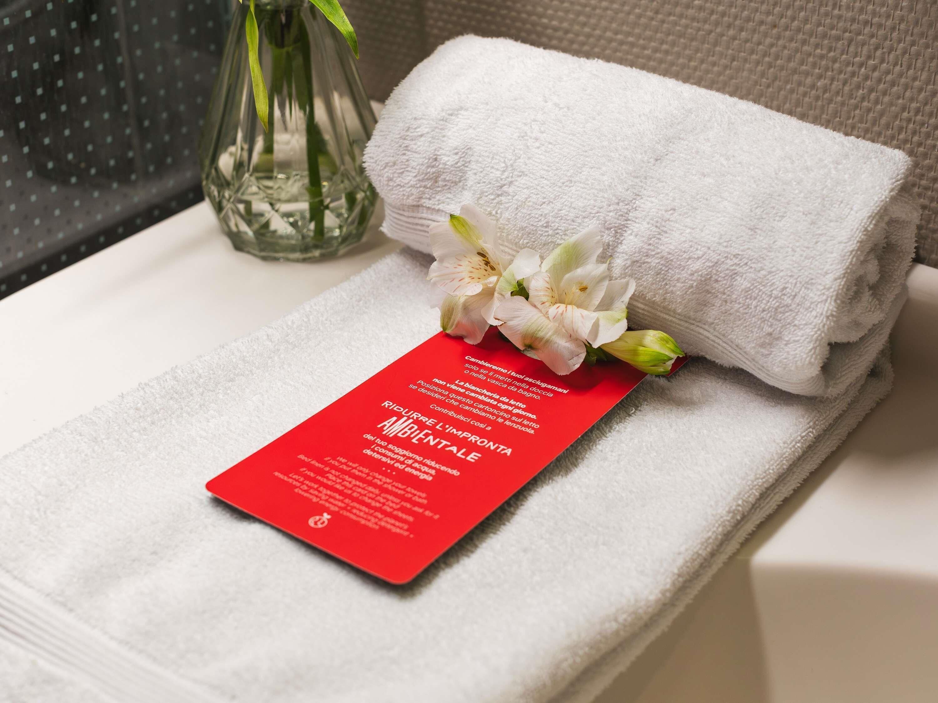 A neatly folded white towel with a red card and white flowers on a white surface.