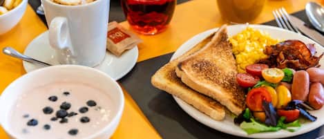 A breakfast setting with toast, eggs, sausages, and a bowl of yogurt with blueberries.