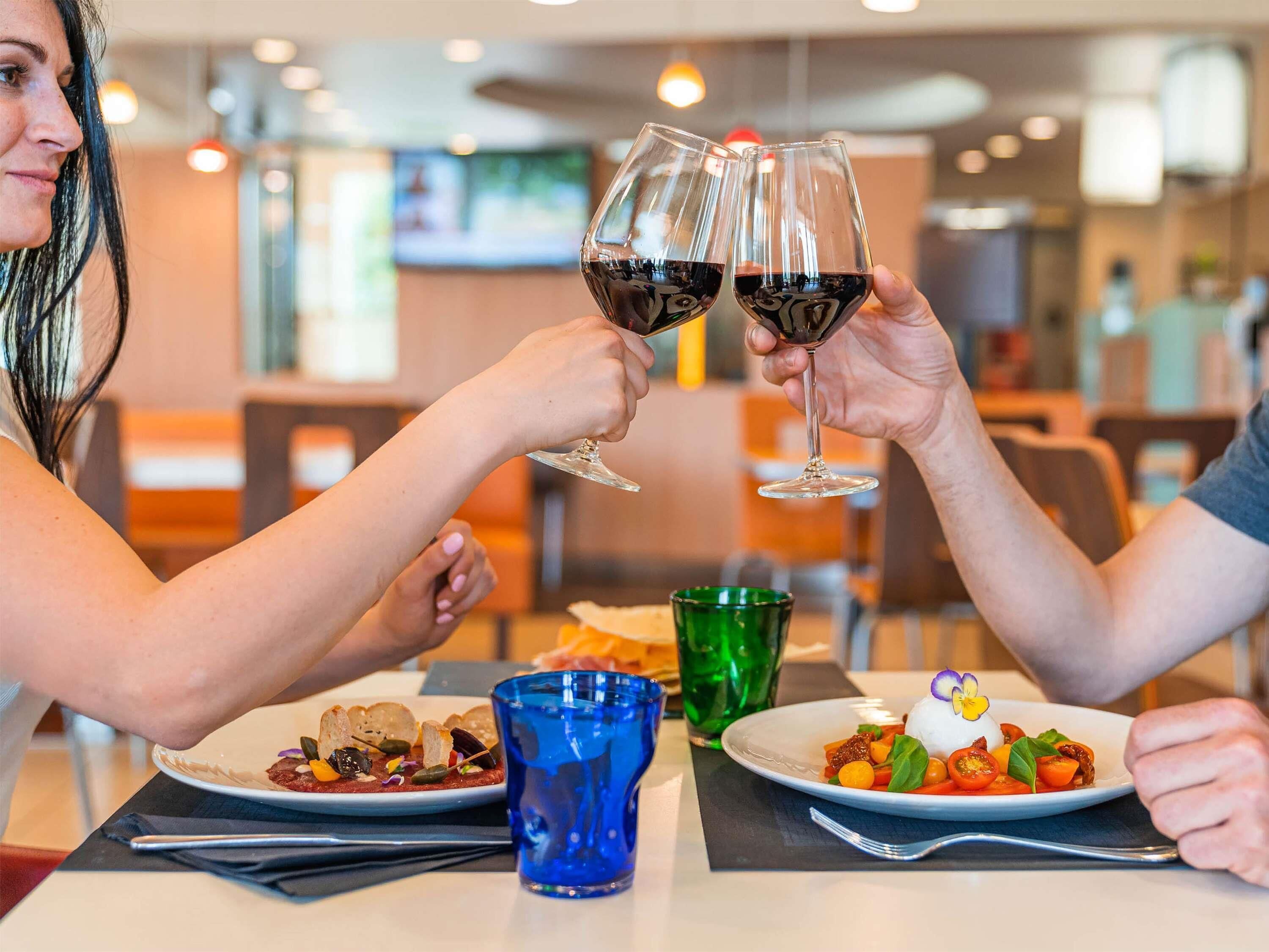 A dining table with plates of food, glasses of red wine, and a blue glass.